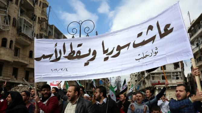 Syrian civilians and activists hold a banner reading in Arabic "Long live Syria, down with Assad" during an anti-regime demonstration in the rebel-controlled side of Aleppo, on March 4, 2016